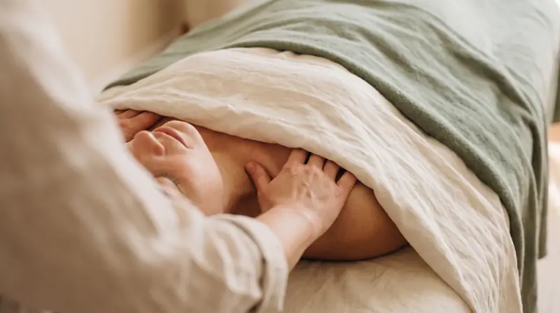 Close-up of a gentle lymphatic drainage massage technique at the neck and collarbone, client lying face-up